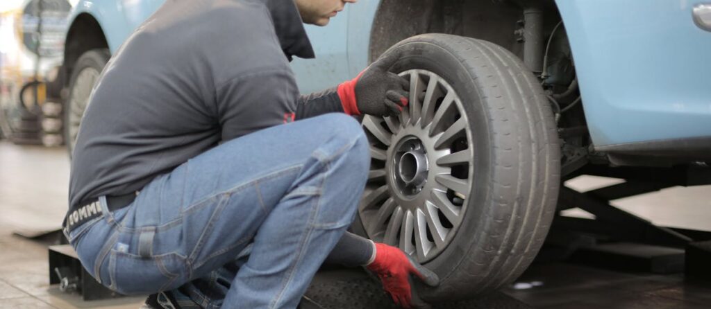 Mechanic changing a car tire indoors, using tools for vehicle maintenance.